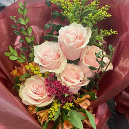 Bouquet of pale pink roses with mixed filler flowers wrapped in burgundy paper