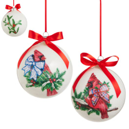 Three white Christmas ornaments with red bows and cardinal designs