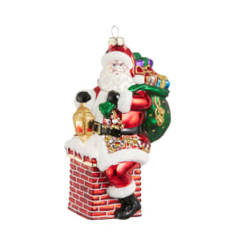 Santa ornament sitting on a brick chimney with gifts and a lantern