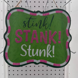 Green hanging sign with pink glitter trim reading "stink! STANK! Stunk!"