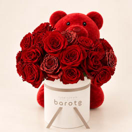 Red rose bouquet in a white box with a large red teddy bear behind it