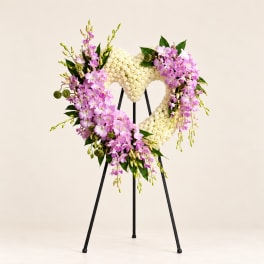 Heart-shaped floral wreath with pink orchids and white flowers on a stand
