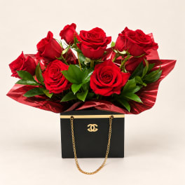 Red roses arranged in a black gift box with gold chain handles