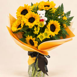 Bouquet of sunflowers with a small teddy bear in a glass vase