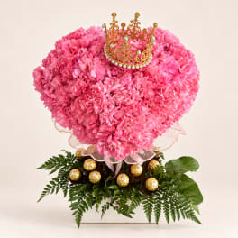 Pink floral heart arrangement topped with a gold crown and surrounded by chocolates