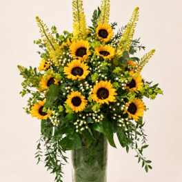 Sunflower arrangement in a tall glass vase with yellow spikes and white berries