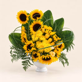 Sunflower and yellow rose arrangement in a white pedestal vase