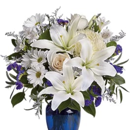 White lilies and daisies arranged in a blue glass vase