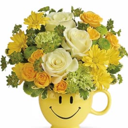 Yellow and white flower arrangement in a smiley-face mug