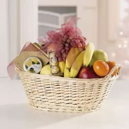 Fruit basket with bananas, grapes, oranges, and packaged sweets in a wicker basket