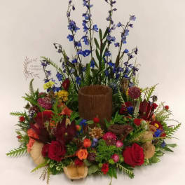 Colorful floral arrangement with red roses and tall blue flowers in a wooden container