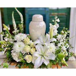 White floral arrangement with lilies, roses, and chrysanthemums around a ceramic urn