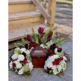 Floral funeral urn arrangement with white and deep red flowers around a wooden box