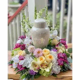 Floral wreath around a white urn with pink, yellow, and white blooms