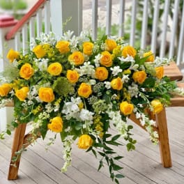 Yellow rose and white flower arrangement draped over a wooden bench