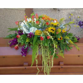 Large colorful floral arrangement with sunflowers and tulips in a wooden casket spray