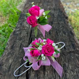Pink rose corsage and boutonniere with ribbon on a wooden bench