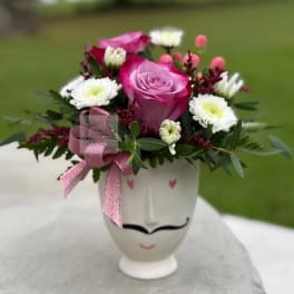 Pink rose and white daisy bouquet in a white face vase with a pink ribbon