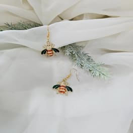 Pair of bee-shaped drop earrings on white fabric with faux greenery