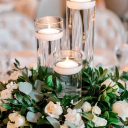 White roses and greenery surround three glass candle cylinders