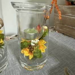 Glass hurricane vase with a small candle and yellow floral accents
