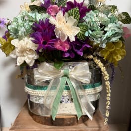 Mixed bouquet of purple, cream, and mint flowers in a decorated metal container