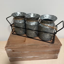 Three galvanized metal vases in a black wire caddy on a wooden box