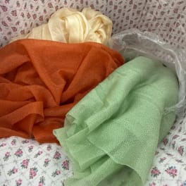 Three folded rolls of sheer fabric in cream, orange, and green