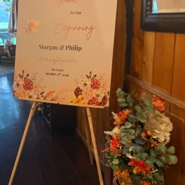 Floral arrangement beside a wedding welcome sign on an easel