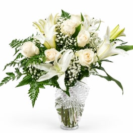 White lilies and roses in a clear glass vase with baby's breath