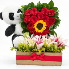 Panda plush beside red roses and lilies in a wooden box with a red ribbon