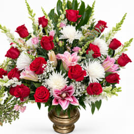 Large bouquet of red and pink roses with white blooms in a gold vase