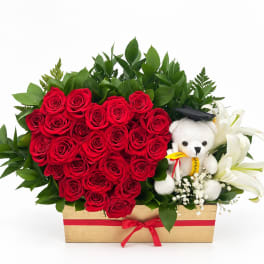 Heart-shaped red rose arrangement with white lilies and a teddy bear in a wooden box
