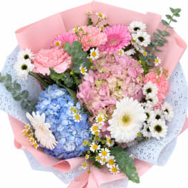 Pastel bouquet of hydrangeas, gerbera daisies, and small white daisies in pink wrap