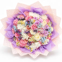 Round bouquet of pink, white, and purple flowers wrapped in lavender paper