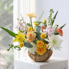 Mixed bouquet in a woven basket with yellow, white, and pink flowers