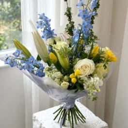 Bouquet of blue delphinium, white roses, and yellow tulips wrapped in pale paper