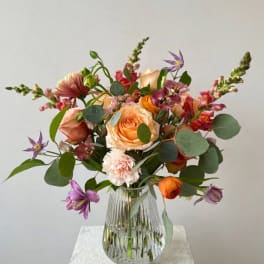 Mixed bouquet of peach, pink, and purple flowers in a glass vase