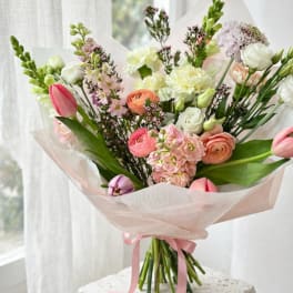 Pastel bouquet of mixed flowers wrapped in pink paper with a ribbon