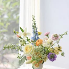Mixed pastel flower arrangement in a white vase by a window