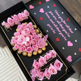 Pink roses arranged in a black gift box with chocolates and butterfly decorations