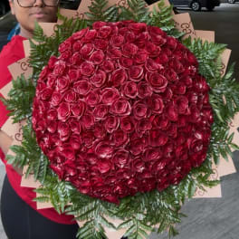 Large bouquet of red roses with fern foliage, held by a person