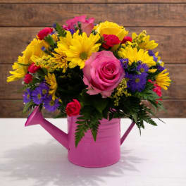 Bright mixed bouquet in a pink watering can vase