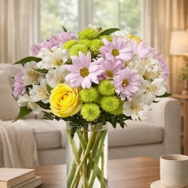 Bouquet of pink daisies, white alstroemeria, and yellow roses in a glass vase.