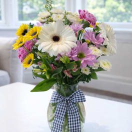 Mixed bouquet of daisies and sunflowers in a glass vase with a checkered ribbon