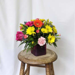 Colorful mixed bouquet in a dark square vase on a wooden stool