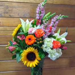 Mixed bouquet with sunflowers, roses, lilies, and hydrangeas in a glass vase