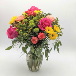 Mixed bouquet of pink roses, yellow daisies, and carnations in a glass vase