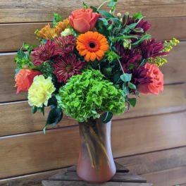Mixed bouquet of orange, pink, purple, and green flowers in a glass vase
