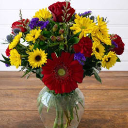 Mixed bouquet of red, yellow, and purple flowers in a clear glass vase